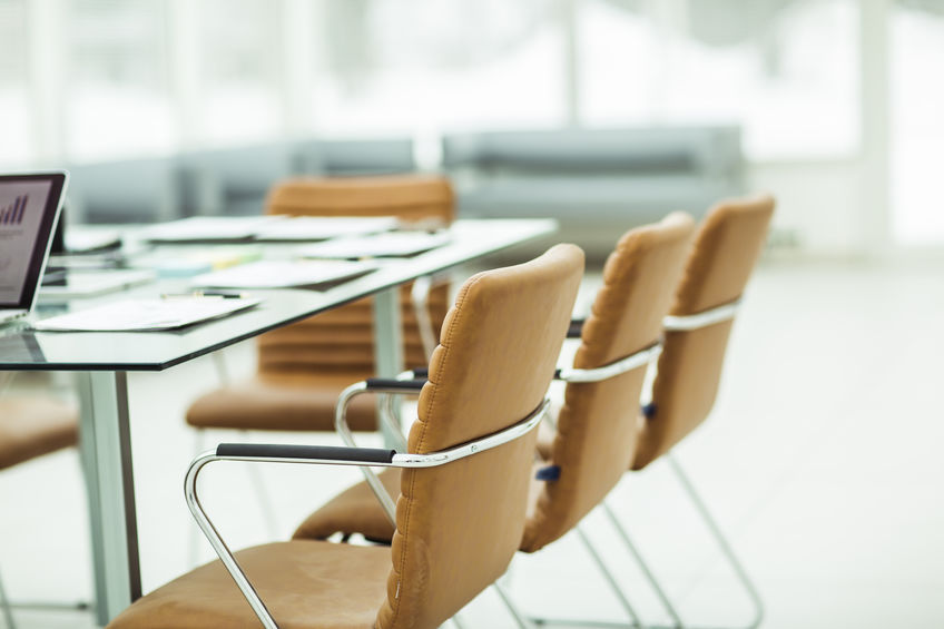 Conference table with tan chairs, papers, and a laptop in a bright, modern office setting.